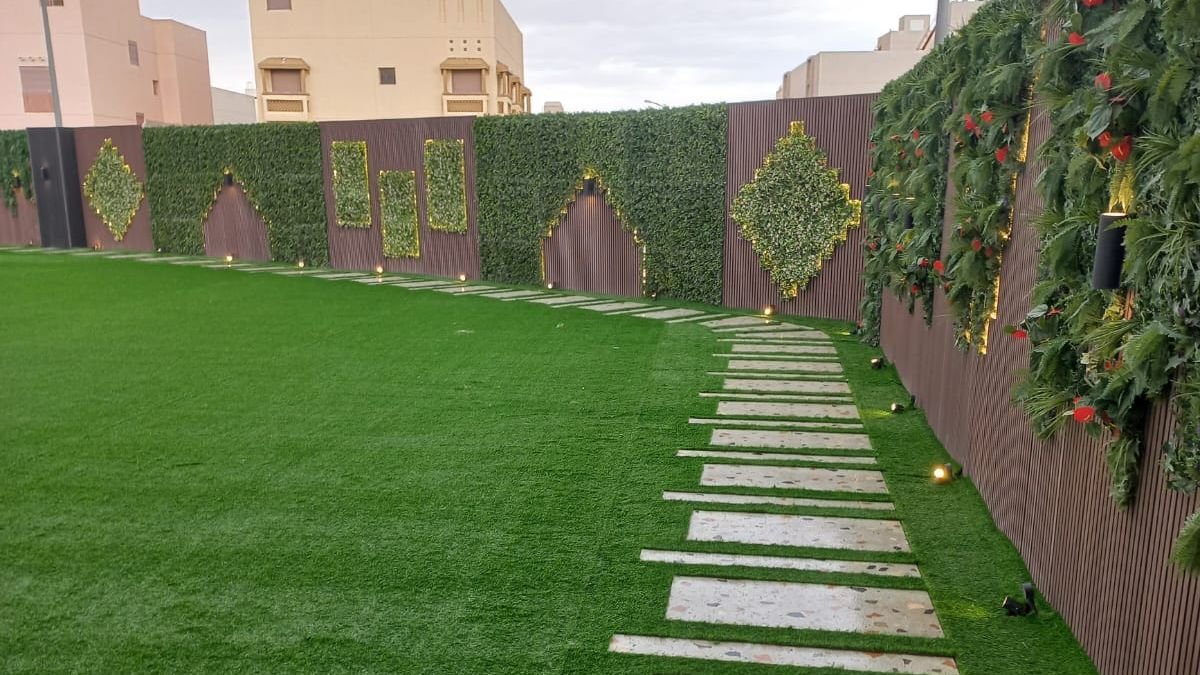 عشب صناعي مع ممر بلاط وجدار أخضر مضاء في حديقة بالرياض
